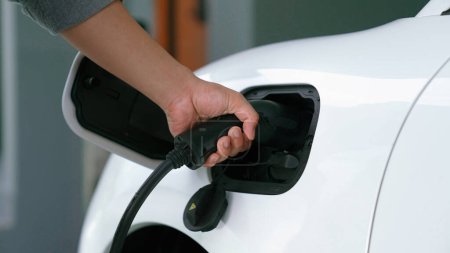 Photo for Progressive man attaches an emission-free power connector to the battery of electric vehicle at his home. Electric vehicle charging via cable from charging station to EV car battery - Royalty Free Image