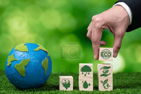 Photo for Businessman hand holding wooden cube with eco symbol and paper globe on fertile soil background. Environmental awareness and sustainable energy. Clean and renewable energy for greener ecology. Alter - Royalty Free Image