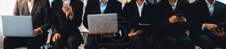 Photo for Asian job applicant in identical formal wear sitting in waiting room for job interview. Office worker or business people working in cramped room together using laptop and phone. Trailblazing - Royalty Free Image