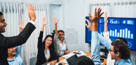 Téléchargez les photos : Groupe de gens d'affaires multiethniques heureux dans le geste de célébration et le travail d'équipe réussie après avoir fait des ventes de succès ou affichage positif du tableau de bord des données financières à l'écran dans la salle de réunion. Habillement - en image libre de droit