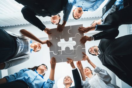 Photo for Multiethnic business people holding jigsaw pieces and merge them together as effective solution solving teamwork, shared vision and common goal combining diverse talent. Below view. Habiliment - Royalty Free Image
