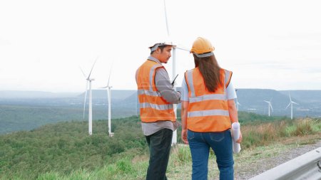 Téléchargez les photos : Ingénieurs et ingénieures travaillant dans un parc éolien au sommet d'une colline ou d'une montagne en milieu rural. Idéal progressif pour la production future d'énergie renouvelable et durable. - en image libre de droit