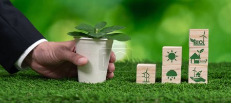 Photo for Businessmans hand holding eco-concern symbol on wooden cube and plant pot. Eco-friendly bio fuel from plants or waste for alternative sustainable and clean bio energy to preserve eco future. Alter - Royalty Free Image