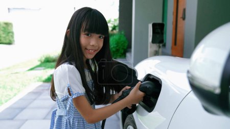 Foto de Una chica juguetona sosteniendo un enchufe EV, una estación de carga doméstica que proporciona una fuente de energía sostenible para los vehículos eléctricos. Energía alternativa para un estilo de vida progresivo. - Imagen libre de derechos