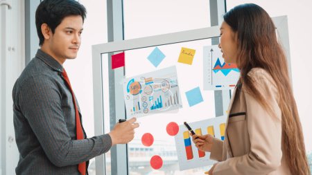 Photo for Business people work on project planning board in office and having conversation with coworker friend to analyze project development . They use sticky notes posted on glass to make it organized. Jivy - Royalty Free Image