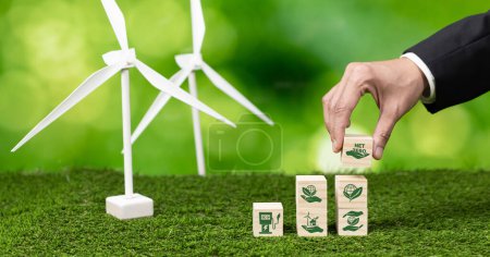Photo for Businessman putting Net Zero symbol cube on stack top for corporate use eco-friendly energy and sustainability. Wind turbine generate renewable and clean energy with net zero CO2 emission. Alter - Royalty Free Image