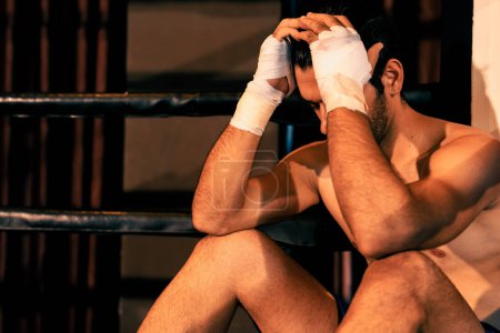 Téléchargez les photos : Fatigué et épuisé boxeur caucasien enlevé son gant de boxe et assis, reposant sur le bord de l'anneau après un entraînement intense ou un match de combat. Impulsion - en image libre de droit