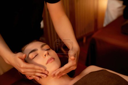 Téléchargez les photos : Femme caucasienne profiter relaxant anti-stress massage de la tête et choyer beauté faciale loisirs de la peau dans la bougie chaude éclairage spa salon ambiant dans un complexe de luxe ou un hôtel. Tranquillité - en image libre de droit