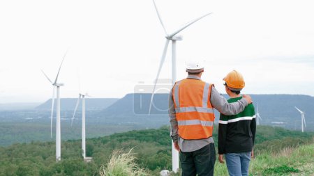 Foto de Ingeniero con su hijo en un parque eólico en lo alto de una colina o montaña en el campo. Ideales progresivos para la producción futura de energía renovable y sostenible. Generación de energía a partir de turbina eólica. - Imagen libre de derechos