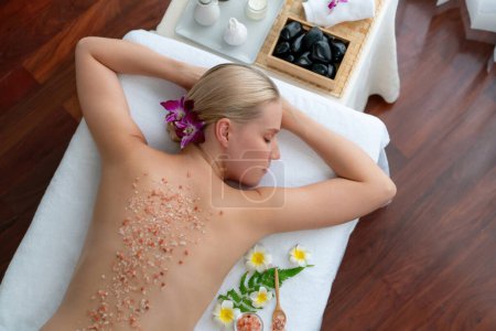 Photo for Panorama top view woman customer having exfoliation treatment in luxury spa salon with warmth candle light ambient. Salt scrub beauty treatment in health spa body scrub. Quiescent - Royalty Free Image