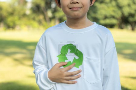 Foto de Joven niño asiático alegre sosteniendo símbolo de reciclaje en el parque verde natural de luz natural que promueve el reciclaje de residuos, reducir y reutilizar el estímulo para la conciencia ecológica sostenible para la generación futura. Gyre. - Imagen libre de derechos