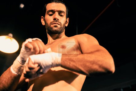 Téléchargez les photos : Portrait de boxeur caucasien avec corps musclé et athlétique enveloppant sa main ou son poing sur le ring avant le match ou l'entraînement de combat de boxe. Impulsion - en image libre de droit