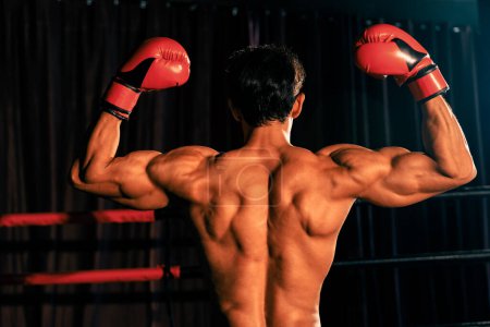 Téléchargez les photos : Vue arrière du boxeur thaïlandais victorieux Muay frappe pose triomphante, se prélassant dans la gloire de sa victoire durement gagnée affichant fièrement son corps fort et musclé. Impulsion - en image libre de droit