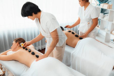Photo for Hot stone massage at spa salon in luxury resort with day light serenity ambient, blissful couple customer enjoying spa basalt stone massage glide over body with soothing warmth. Quiescent - Royalty Free Image