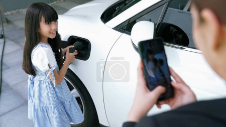Photo for Progressive lifestyle of mother and daughter who have just returned from school in an electric vehicle that is being charged at home. Electric vehicle powered by sustainable clean energy. - Royalty Free Image