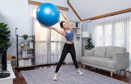 Foto de Joven atractiva mujer asiática en ropa deportiva mantenga y levante la bola en forma dirigida en el músculo abdominales para una rutina de ejercicios en casa enérgica eficaz. Vigoroso - Imagen libre de derechos