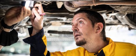Photo for Vehicle mechanic conduct car inspection from beneath lifted vehicle. Automotive service technician in uniform carefully diagnosing and checking cars axles and undercarriage components. Panorama Oxus - Royalty Free Image