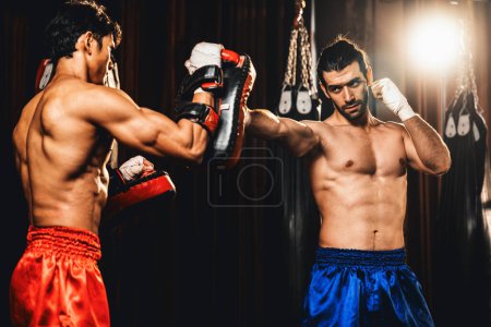 Téléchargez les photos : Le boxeur asiatique et caucasien Muay Thai déchaîne le punch lors d'une séance d'entraînement de boxe féroce, offrant une frappe de poinçon à l'entraîneur de sparring, mettant en valeur la technique et les compétences de boxe thaïlandaise Muay. Impulsion - en image libre de droit