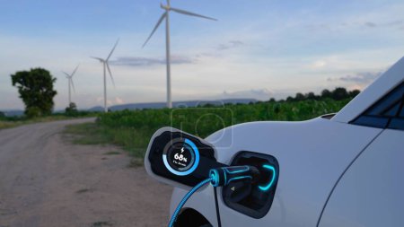 Téléchargez les photos : L'énergie de recharge de voiture électrique de la station de charge EV affiche l'hologramme futuriste d'état de batterie intelligente par le câble de prise de chargeur EV dans le parc d'éoliennes. Durabilité des énergies propres alternatives. Pertinence - en image libre de droit