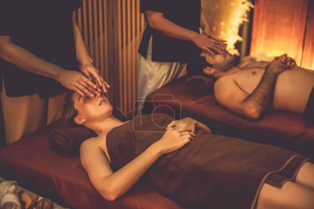Foto de Pareja de clientes disfrutando de relajantes masajes anti-estrés en la cabeza y mimar la belleza facial recreación de la piel de ocio en el cálido salón de iluminación de velas spa ambiente en un resort de lujo u hotel. Silencioso. - Imagen libre de derechos
