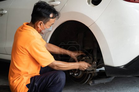 Téléchargez les photos : Mécanicien travailleur changer de roue de voiture dans l'atelier de réparation automobile. Travailleur d'entretien automobile changer les pneus en caoutchouc qui fuient dans le concept d'entretien de voiture professionnelle et d'entretien. Oxus - en image libre de droit