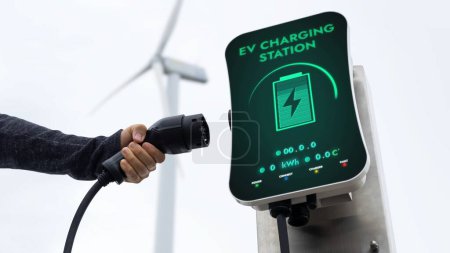 Téléchargez les photos : Chargeur EV de la station de recharge de voiture EV dans la nature et parc d'éoliennes réduisant les émissions de CO2. Avancement technologique de la durabilité des énergies alternatives et de la voiture électrique. Pertinence - en image libre de droit
