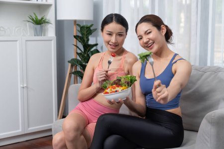 Photo for Young sporty Asian women in sportswear holding salad bowl together fill with vibrant of fruit and vegetable. Natural youthful and fit body lifestyle with balance nutrition and home exercise. Vigorous - Royalty Free Image