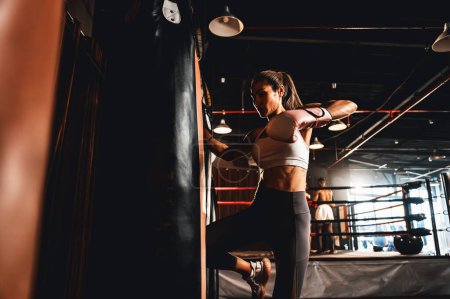 Foto de Mujer asiática boxeadora Muay Thai con un fuerte cuerpo atlético y muscular utilizando su rodilla y puño saco de boxeo como su entrenamiento de boxeo en el gimnasio. Arte marcial y estilo de vida deportivo. Impulso - Imagen libre de derechos