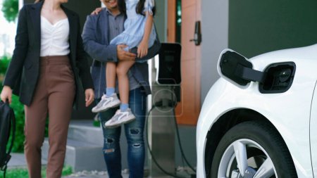 Photo for Progressive young parents and daughter living in a home with an electric vehicle and electronic vehicle charging station. Green and clean energy from electric vehicles for healthy environment. - Royalty Free Image