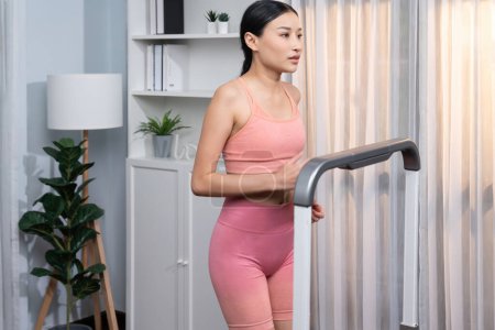 Photo for Energetic and strong athletic asian woman running running machine at home. Pursuit of fit physique and commitment to healthy lifestyle with home workout and training. Vigorous - Royalty Free Image