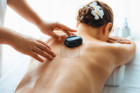 Photo for Hot stone massage at spa salon in luxury resort with day light serenity ambient, blissful woman customer enjoying spa basalt stone massage glide over body with soothing warmth. Quiescent - Royalty Free Image