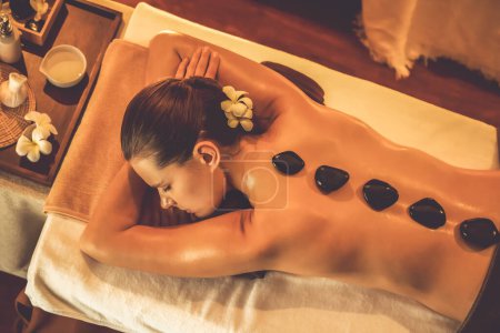 Photo for Panorama top view hot stone massage at spa salon in luxury resort with warm candle light, blissful woman customer enjoying spa basalt stone massage glide over body with soothing warmth. Quiescent - Royalty Free Image