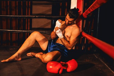 Téléchargez les photos : Boxeur caucasien avec douleur et blessure après un entraînement de boxe intense ou un match de combat, assis au bord de l'anneau. Blessures physiques dans le sport concept. Impulsion - en image libre de droit