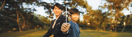 Téléchargez les photos : Asian boy and businessman hold wind turbine model together as corporate social responsible to make more green by eco alternative energy for sustainable future generation. Panorama arrière-plan flou.Gyre - en image libre de droit
