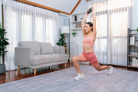 Photo for Vigorous energetic woman doing yoga and weight lifting exercise at home. Young athletic asian woman strength and endurance training session as home workout routine. - Royalty Free Image