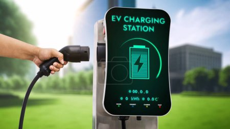Téléchargez les photos : Homme d'affaires tirer chargeur EV pour recharger sa batterie de voitures électriques à partir de la station de charge en arrière-plan vert éco parc de la ville. Futur véhicule électrique innovant et durabilité énergétique. Pertinence - en image libre de droit