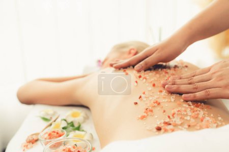 Photo for Closeup woman customer having exfoliation treatment in luxury spa salon with warmth candle light ambient. Salt scrub beauty treatment in health spa body scrub. Quiescent - Royalty Free Image