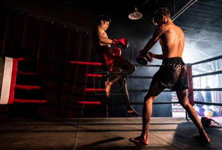 Foto de El boxeador asiático y caucásico Muay Thai desencadena un ataque de rodilla en una feroz sesión de entrenamiento de boxeo, entregando un golpe de rodilla al entrenador de sparring, mostrando la técnica y habilidad de boxeo Muay Thai. Impulso - Imagen libre de derechos