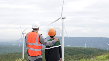 Foto de Ingeniero con su hijo en un parque eólico en lo alto de una colina o montaña en el campo. Ideales progresivos para la producción futura de energía renovable y sostenible. Generación de energía a partir de turbina eólica. - Imagen libre de derechos