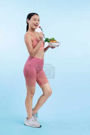 Photo for Young sporty Asian woman in sportswear holding salad bowl fill with vibrant of fruit and vegetable. Natural youthful and fit body lifestyle with balance nutrition on isolated background. Vigorous - Royalty Free Image