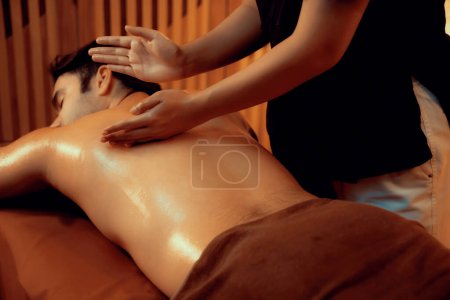 Téléchargez les photos : Homme caucasien client appréciant relaxant massage spa anti-stress et dorloter avec beauté loisirs de la peau dans la bougie chaude éclairage spa salon ambiant à la station de luxe ou hôtel. Tranquillité - en image libre de droit