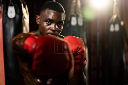 Photo for Boxing fighter shirtless posing, African American Black boxer punch his fist in aggressive stance and ready to fight at gym with kicking bag and boxing equipment in background. Impetus - Royalty Free Image