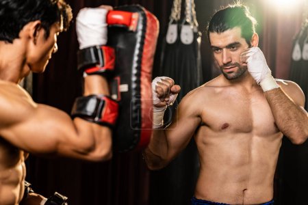 Téléchargez les photos : Le boxeur asiatique et caucasien Muay Thai déchaîne le punch lors d'une séance d'entraînement de boxe féroce, offrant une frappe de poinçon à l'entraîneur de sparring, mettant en valeur la technique et les compétences de boxe thaïlandaise Muay. Impulsion - en image libre de droit