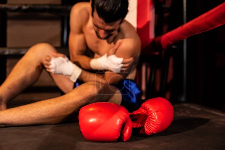 Téléchargez les photos : Boxeur caucasien avec douleur et blessure après un entraînement de boxe intense ou un match de combat, assis au bord de l'anneau. Blessures physiques dans le sport concept. Impulsion - en image libre de droit