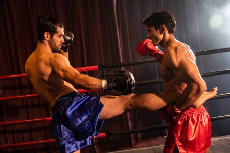 Téléchargez les photos : Le boxeur asiatique et caucasien Muay Thai lance une attaque de coups de pied dans un match de boxe féroce tandis que le concurrent en position défensive tient la jambe de coups de pied avec des prouesses de combat implacables. Impulsion - en image libre de droit