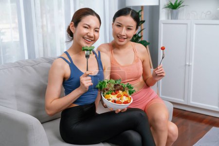 Téléchargez les photos : Jeunes femmes asiatiques sportives en vêtements de sport tenant saladier remplir ensemble avec vibrant de fruits et légumes. Style de vie corporel naturel jeune et en forme avec équilibre nutritionnel et exercice à la maison. Vigoureux - en image libre de droit