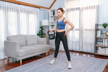 Photo for Vigorous energetic woman doing kettlebell weight lifting exercise at home. Young athletic asian woman strength and endurance training session as home workout routine. - Royalty Free Image