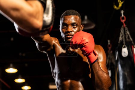 Foto de Boxeador negro afroamericano que golpea en el entrenador o entrenador que usa guantes de perforación como equipo de entrenamiento de bolsa de boxeo en el gimnasio. Entrenamiento de fuerza y resistencia para un combate de boxeo profesional. Impulso - Imagen libre de derechos