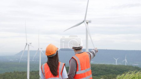Photo for Male and female engineers working on a wind farm atop a hill or mountain in the rural. Progressive ideal for the future production of renewable, sustainable energy. - Royalty Free Image