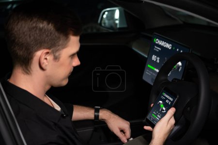 Photo for Electric car driver checks battery charging status, range and charging limit on app screen in the car. Smart technology device show EV car recharging data of electric storage in car battery innards. - Royalty Free Image